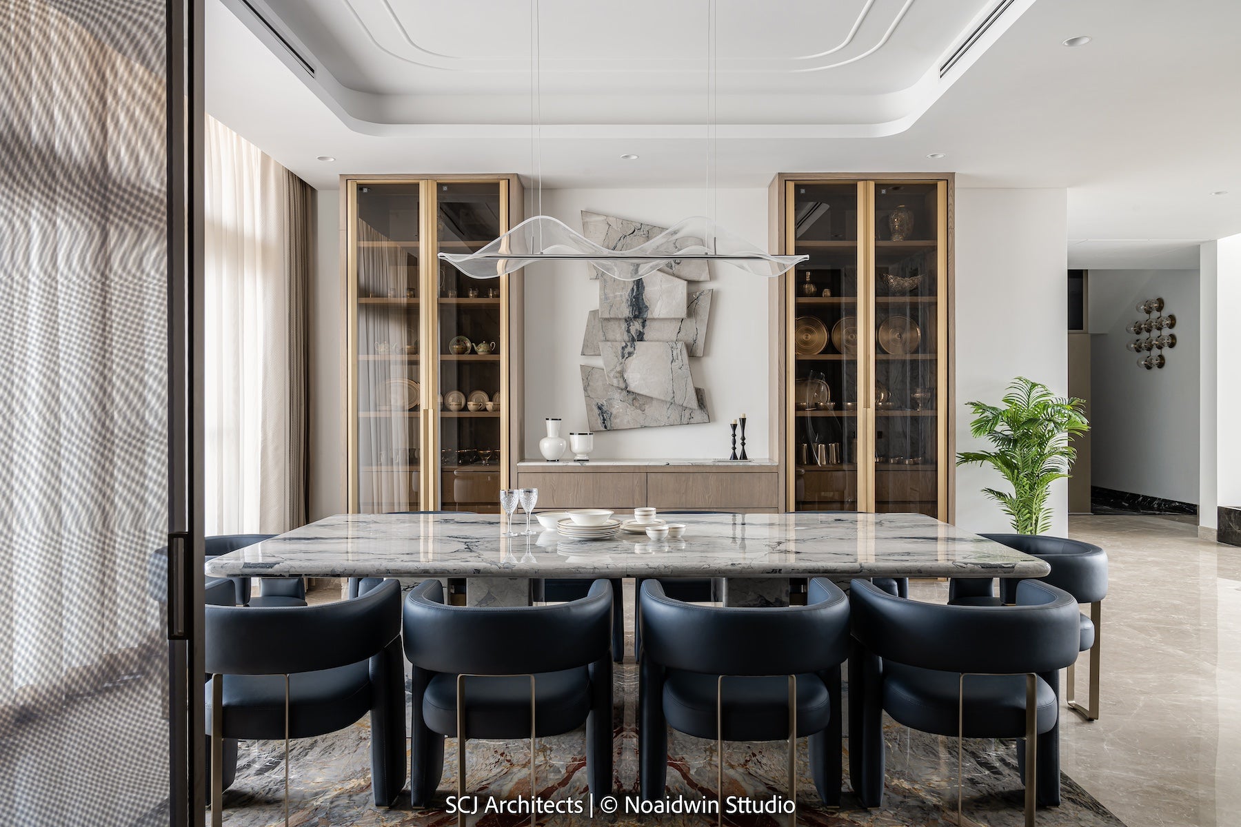 Elegant dining space featuring a sleek marble dining table, leather chairs with gold accents, and curated tableware for luxurious interiors.